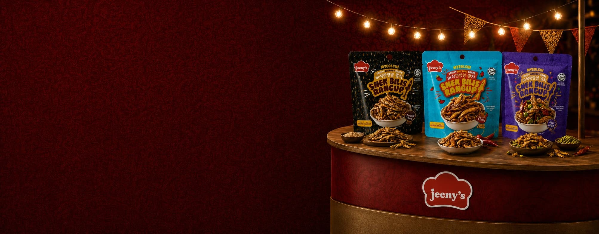 Jeeny's Snek Bilis Rangup crispy anchovy snack packets and sampling bowls on a Jeeny's-branded event counter, under festoon lights and bunting